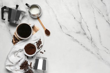 Fincanlı gayzer kahve makinesi, bir sürahi süt, toz ve mermer arka planda fasulye.