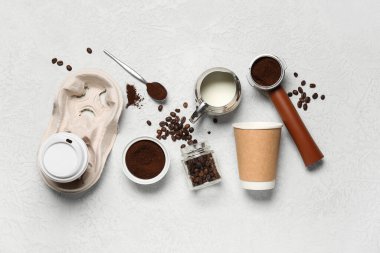 Portafilter, kahve çekirdekleri, toz ve beyaz arka planda sütle servis edilmiş kağıt bardaklar.