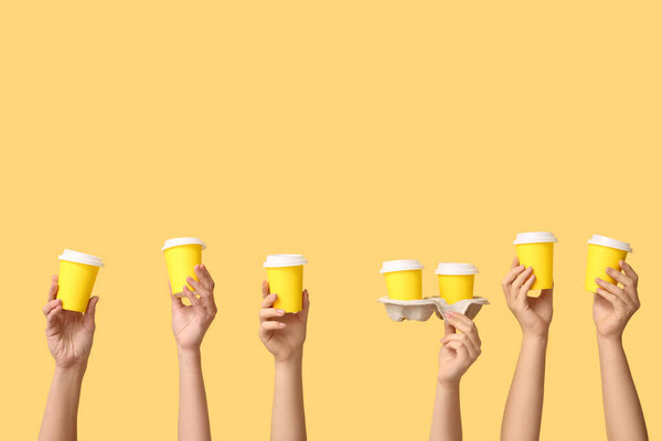 Женские руки с желтыми одноразовыми чашками на цветном фоне