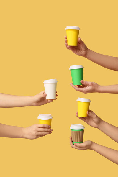 Руки женщины с различными одноразовыми чашками на желтом фоне