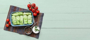 Baking dish with uncooked cabbage rolls, tomatoes, spices and sour cream on wooden background with space for text clipart