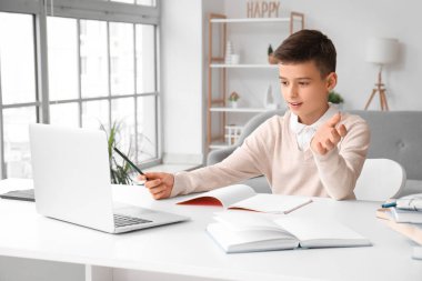 Küçük çocuk evde dizüstü bilgisayarla ders çalışıyor.