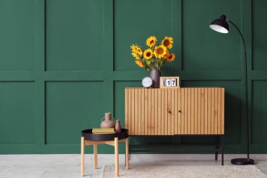 Vase with beautiful sunflowers on wooden cabinet near green wall