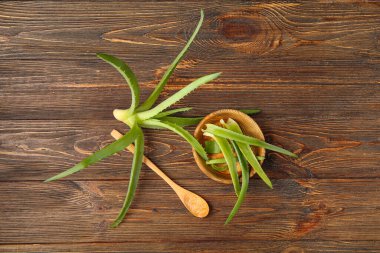 Ahşap arka planda aloe vera yapraklı kaşık ve kase.