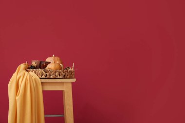 Kavurucu mumlar, kozalaklar, balkabakları ve kırmızı duvarın yanındaki sandalyede sonbahar yapraklarıyla hasır tepsi.