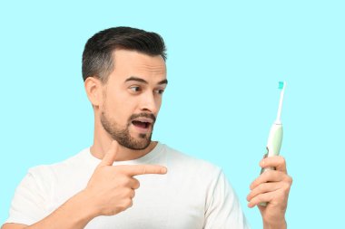Mavi arka planda elektrikli diş fırçasına bakan yakışıklı bir adam.