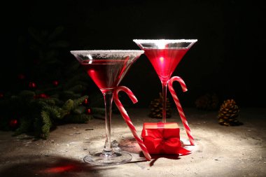 Bir bardak lezzetli kırmızı margarita, baston şekerler ve karanlık arka planda Noel dekoru.