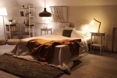 Yatak odasının içinde, yatakta ekose, masalar ve geceleri parlayan lambalar.