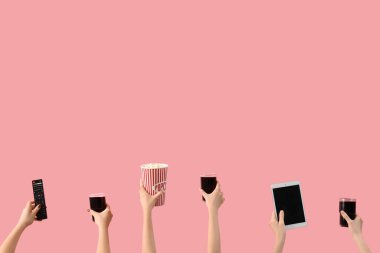 Patlamış mısır, kola, tablet bilgisayar ve pembe arka planda televizyon kumandası tutan eller