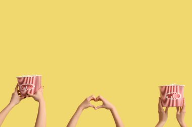 Kovaları patlamış mısırla tutan ve sarı arka planda kalp hareketi gösteren eller.