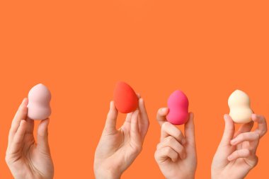 Turuncu arka planda makyaj süngeri olan kadın elleri