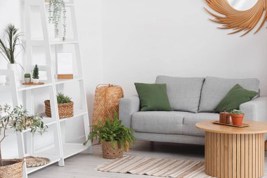 Oturma odasının içinde raf üniteleri, masa, rahat kanepe ve çiçekleri var.