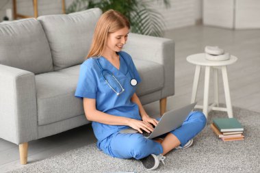 Dizüstü bilgisayarı ve oturma odasında yerde kitapları olan bir kadın stajyer.