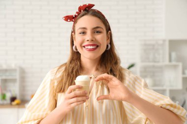 Mutlu gülümseyen genç bir kadın vanilyalı dondurmayı waffle bardağında tutuyor ve evde kalp yapıyor.
