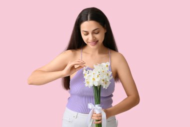 Pembe arka planda bir buket beyaz nergis çiçeğiyle güzel bir genç kadın.