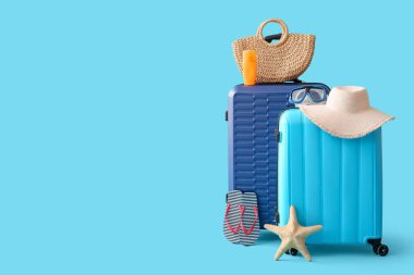 Mavi arka planda deniz yıldızı, hasır çanta, şapka ve plaj aksesuarları olan bavullar.