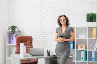 İş yerinin yanında modern bilgisayarlı, gözlüklü, kahve bardaklı, olgun bir iş kadını.