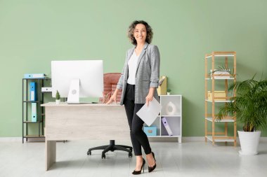 Ofisinde modern bilgisayar olan, iş yerinin yakınında kağıt kağıtları olan olgun, mutlu bir iş kadını.