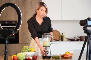 Kadın yemek blogcusu mutfakta video kaydederken sebze smoothie yapıyor