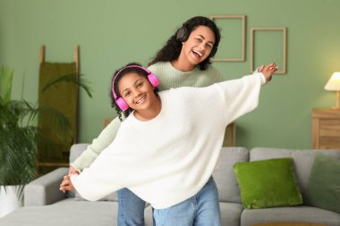 Güzel Afro-Amerikan anne ve kızı kulaklıkla evde müzik dinliyorlar.