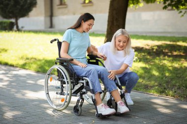 Dışarıda tekerlekli sandalyede kızına yardım eden yaşlı bir kadın.