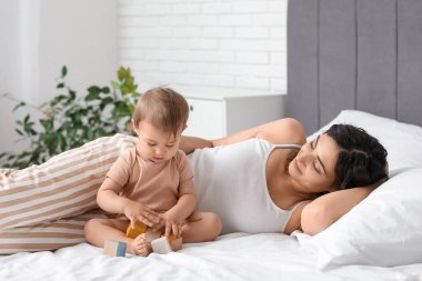 Mutlu anne ve küçük bebeği evde yatakta küplerle oynuyorlar.