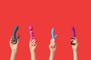 Kırmızı arka planda farklı vibratörlere sahip kadın elleri.