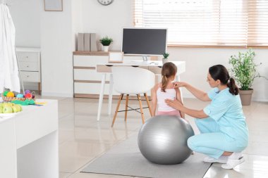 Küçük bir hastası olan kadın osteopat klinikte topa uygun egzersizler yapıyor.