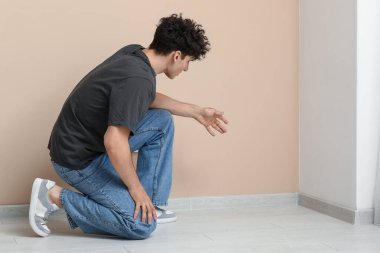 Evdeki bej duvarda küf olan genç adam.