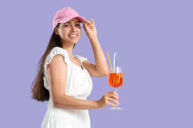 Leylak arka planında aperol sprey kokteyli olan şapkalı genç bir kadın.