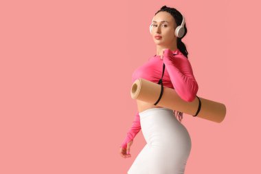 Pembe arka planda fitness paspası olan kulaklıklı bir kadın vücut geliştirici.