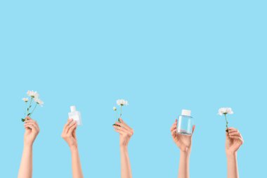 Parfüm şişeleri ve mavi arka planda beyaz çiçekli kadın elleri.