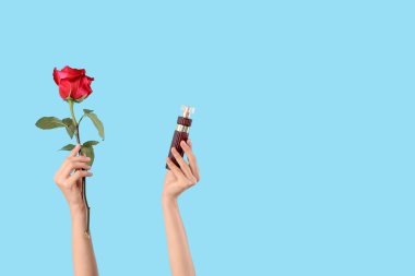 Mavi arka planda parfüm şişesi ve gül çiçekli kadın elleri
