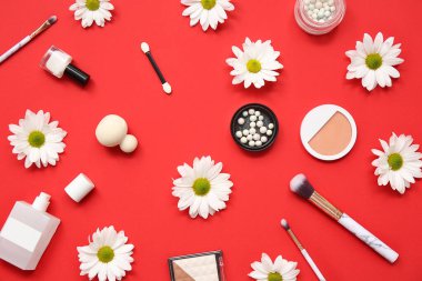 Kırmızı arka planda parfüm, makyaj ürünleri, fırçalar ve çiçeklerle kompozisyon