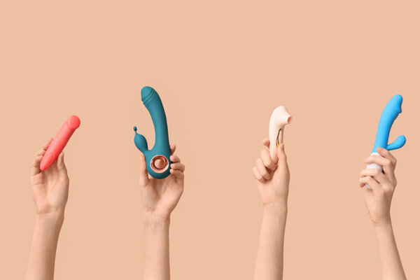 Женские руки с различными вибраторами на коричневом фоне