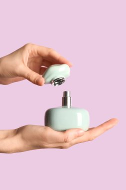 Leylak arka planında yeşil parfüm şişesi olan kadın elleri.