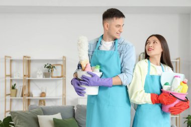 Elektrikli süpürgeyle ve temizlik malzemeleriyle hoş bir çift oturma odasında birbirlerine beşlik çakıyor.