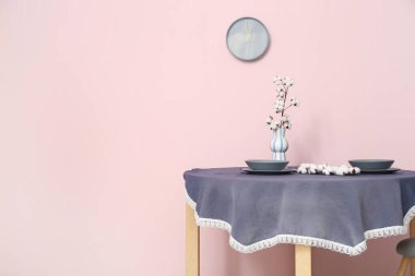 Pamuk çiçekli vazo ve odada pembe duvarın yanında masa örtüsü olan tabaklar.