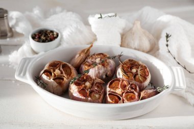 Beyaz ahşap zemin üzerinde sarımsak, biberiye ve kekik ile pişirme tabağı