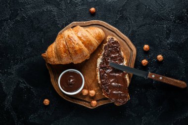 Çikolata kaplı ahşap tahta kruvasan ve siyah arka planda fındık.