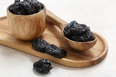 Ahşap kaşık ve kase, beyaz arka planda kuru erik.