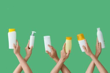 Yeşil arka planda güneş kremi şişeleri olan kadın elleri