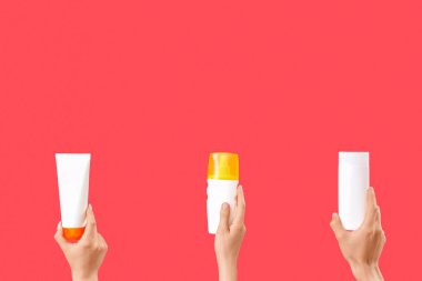 Kırmızı arka planda güneş kremi şişeleri olan kadın elleri.