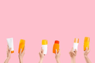 Pembe arka planda güneş kremi şişeleri olan kadın elleri.