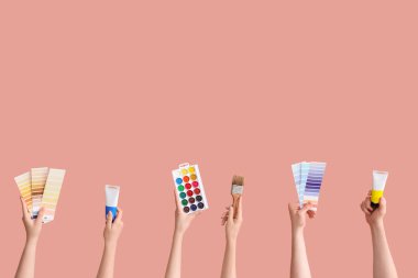 Pembe arka planda sanatçı malzemeleri olan kadın eller.