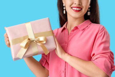 Mavi arka planda hediye kutusu olan güzel genç Asyalı kadın, yakın plan.