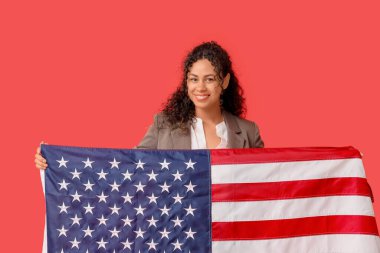 Kırmızı arka planda Amerikan bayrağı olan güzel, mutlu, Afro-Amerikalı bir iş kadını.