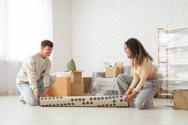 Genç çift yeni dairelerinde eşyalarıyla birlikte kutuların yanına halı koyuyorlar.