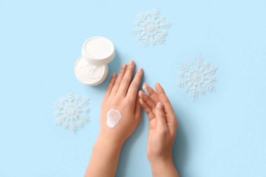 Mavi arka planda kar taneleri olan kozmetik krem süren bir kadın