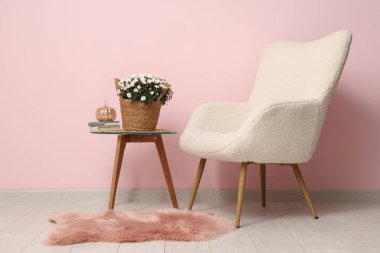 Kahve masasında kasımpatı çiçekleri ve pembe arka planda koltuk olan bir sepet.